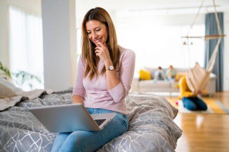 Casual young woman lying on bed and using laptop at home. Technology, people concept